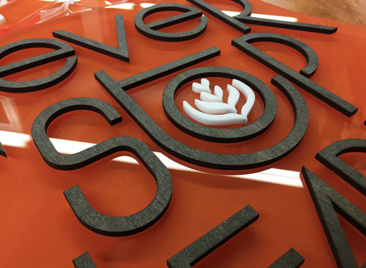 Wall sign with raised black lettering and a white logo mounted on orange acrylic